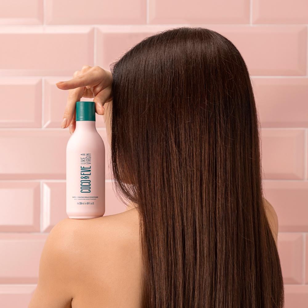 A woman holding the shampoo bottle on her shoulder. 