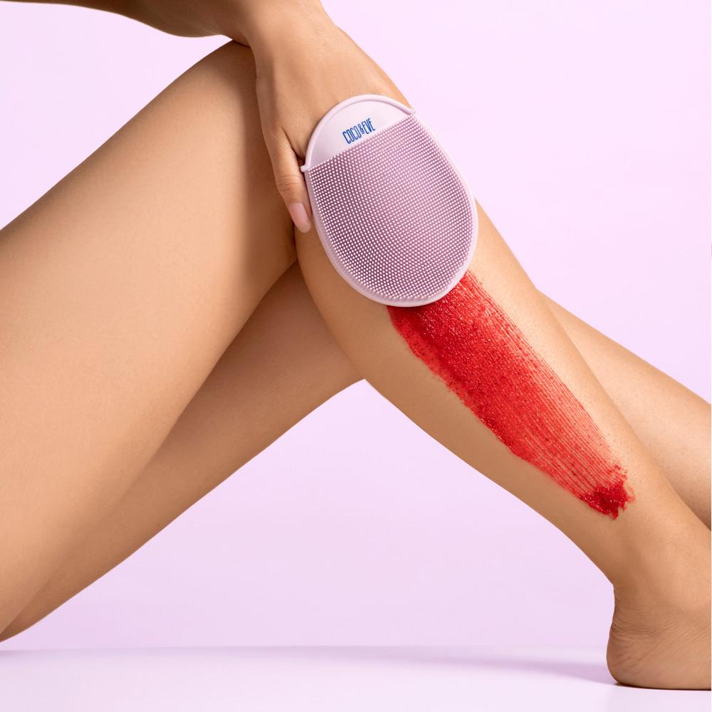 woman rubbing bali buffing sugar on her leg with the exfoliating mitt